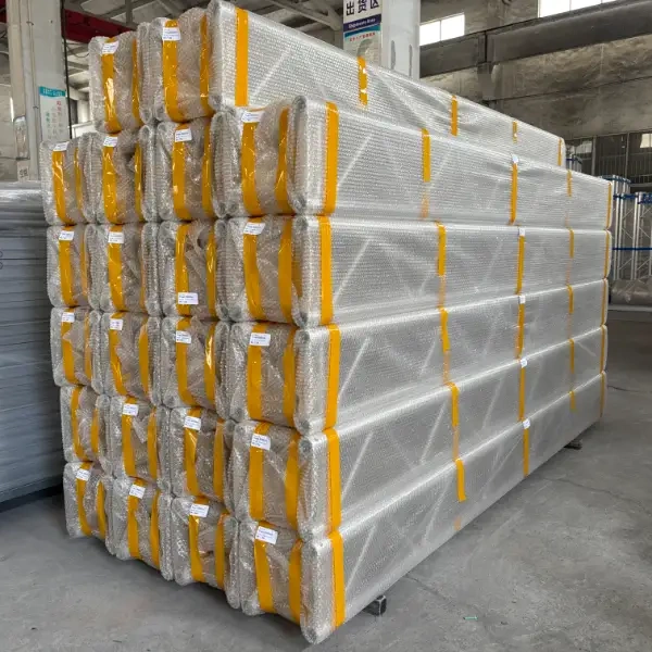 Stacks of aluminum alloy trusses wrapped in double - layer bubble film with yellow straps, stored in an industrial warehouse setting.