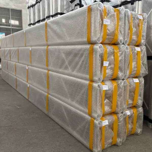 Large stacks of aluminum alloy trusses wrapped in double - layer bubble film and secured with yellow straps, stored in an industrial warehouse.